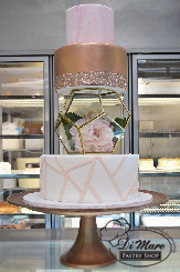 A downright showstopper. This stunning cake has a pink marbled top tier and a gold shimming second tier Those tiers are held up by silk flowers in a terrarium and another tier decorated with a pink abstract design.