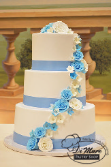 This three their smooth cream frosting with blue ribbon is adorned with a cascade of blue and white gum paste flowers.