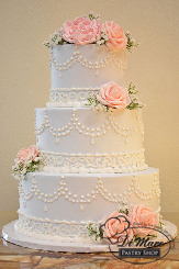 This three tier cream cake has a very Victorian look, it has a lace cream border with a double pearl scallop- fresh flowers accent this traditional cake.