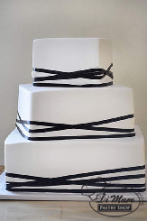 Three tier square caddy corner cake is frosted smooth with cream- geometrical design with a thin black ribbon.