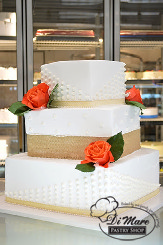 Three tier square cream cake with a rustic design of burlap ribbon and fresh roses.
