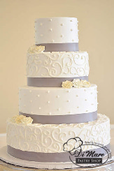 Four tier cream cake with grey ribbon adorned with small white sugar flowers.