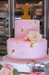 Two tier fondant cake- light pink marbleizing with a geometric design top tier, we accented this cake with gold flakes a gold number 1 ornament and gum paste flower.
