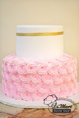 This two tier cake has pink rosettes on the bottom tier, the top tier has a smooth cream frosting and adorned with a thin gold ribbon.