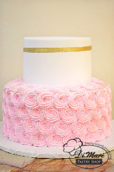 This two tier cake has pink rosettes on the bottom tier, the top tier has a smooth cream frosting and adorned with a thin gold ribbon.